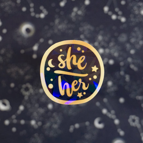gold holo vinyl sticker of the pronouns she her from the shop atelier persephone