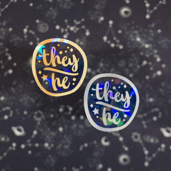 set of two holographic stickers of the lgbt pronouns they he on a starry background from atelier persephone