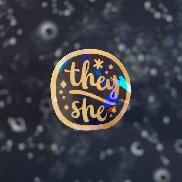 vinyl holographic sticker of the pronoun they she on a dark background with stars