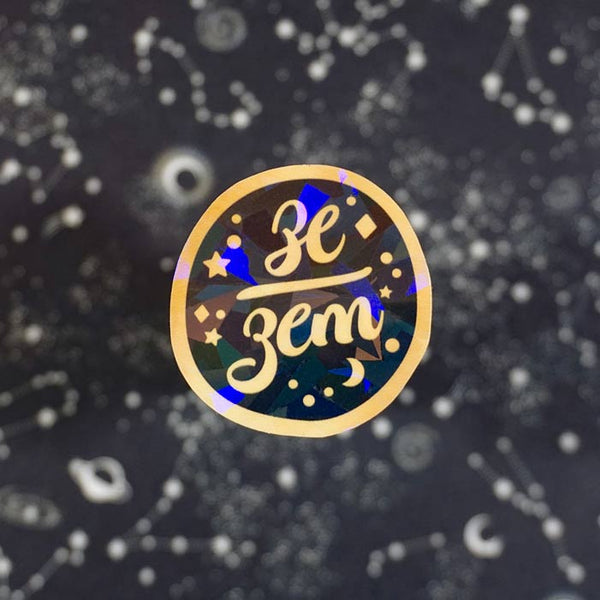 ze zem holographic sticker with gold variant on a starry background made by atelier persephone
